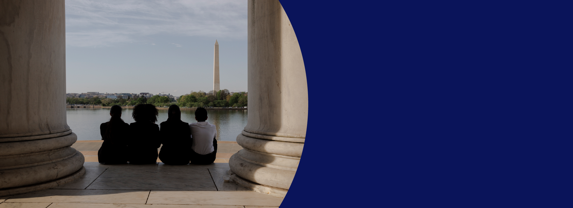 Four people sit together, viewed from behind, framed between two large stone columns. They face a calm body of water, with the Washington Monument standing tall in the distance. The scene feels serene, with soft light casting shadows on the marble floor beneath them. The image captures a moment of reflection, with the iconic monument symbolizing history and unity.