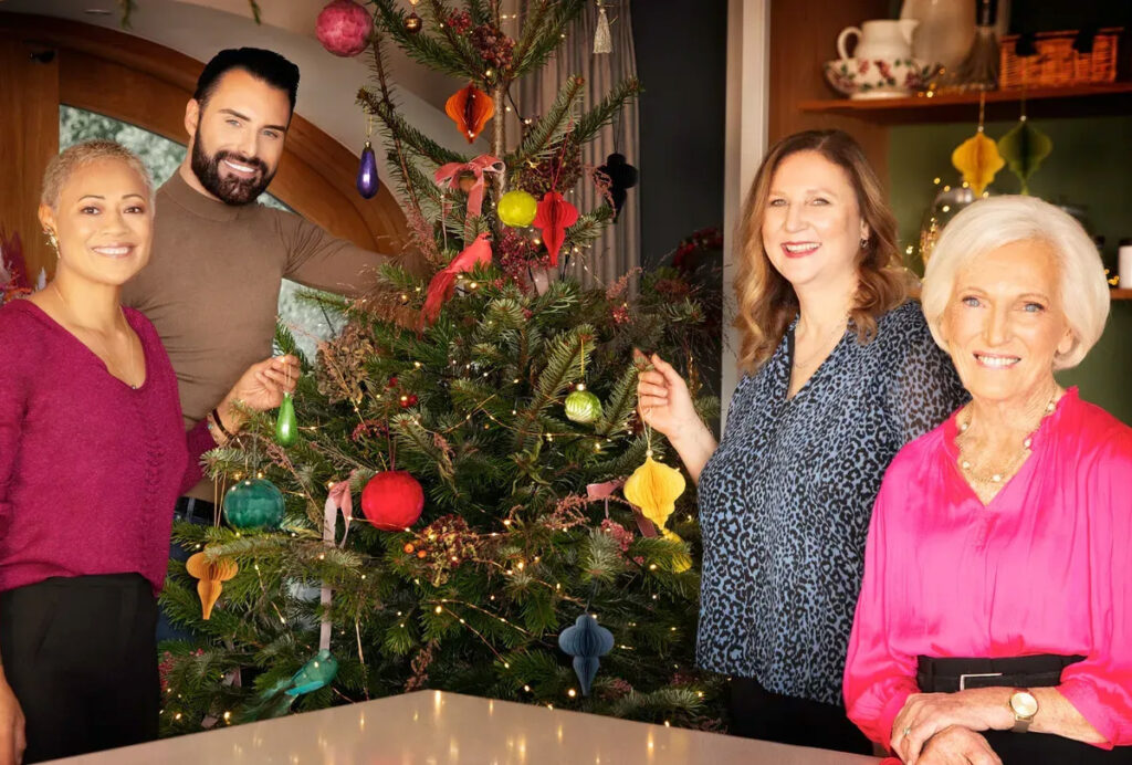 Three women and one man pose in front of a Christmas tree