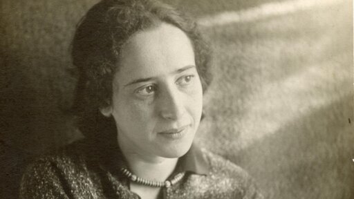 Old black and white photo of a woman standing against a wall and looking off into the distance with a small smile
