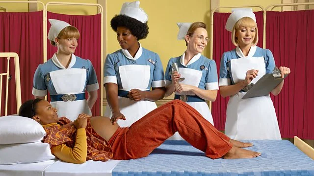Four nurses in 1960's uniform stand in front of a pregnant woman laying on a hospital bed.