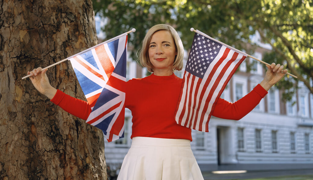 Lucy Worsley stands outside holding two flags; one is an American Flag and the other is Britain's Flag.