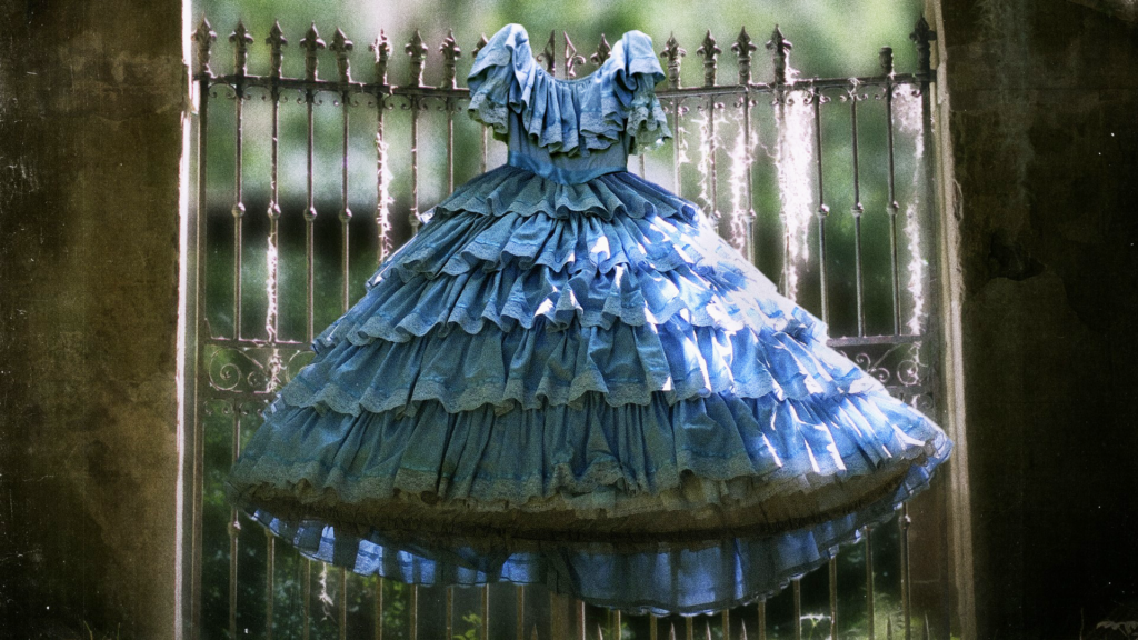 A fancy, blue, southern-style antebellum dress hangs from the spokes of a tall cast-iron fence.