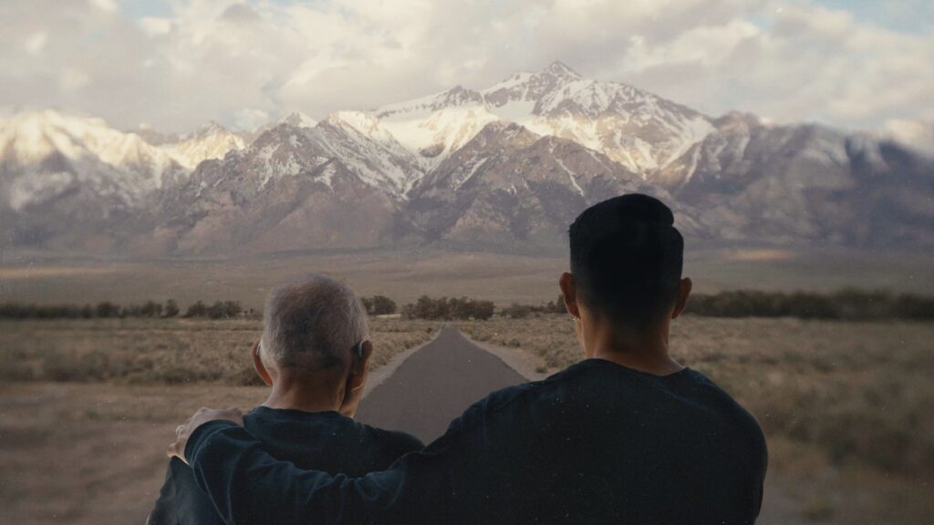 Tadashi Nakamura stands with his arm over his father's shoulder, looking far into the distance at a mountain range.