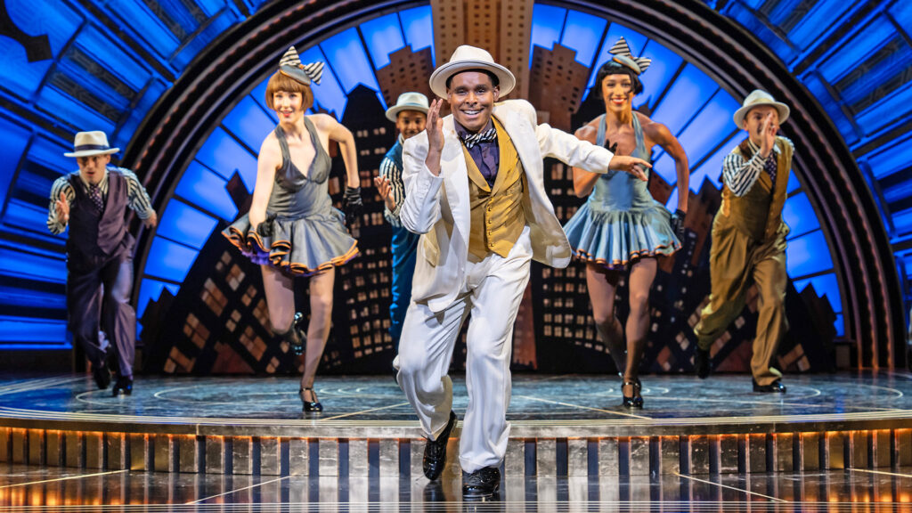 Five dancers glide towards the camera in a musical production of Irving Berlin's Top Hat. They are dressed in 1930's costume.