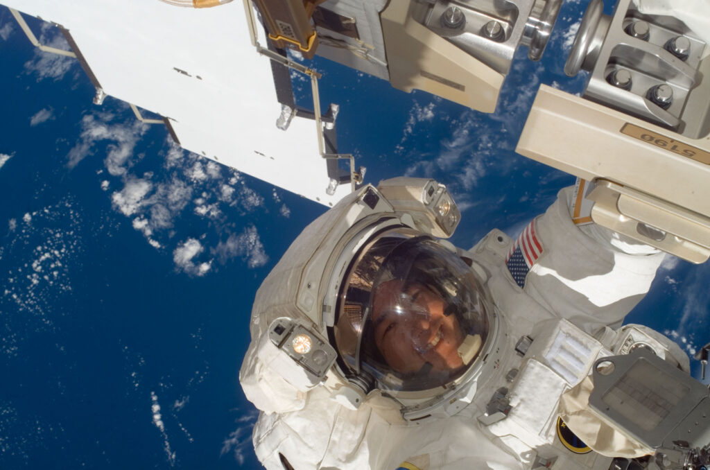An astronaut in a space suit floats in space next to space-equipment.