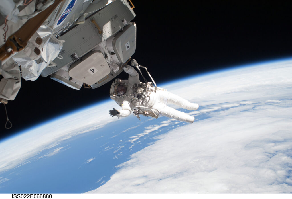 An astronaut in a space suit floats in outer space next to a space ship on the outer layers of earth's atmosphere.
