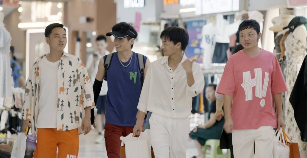 Four young adult men walk through a busy public shopping area together while conversing.