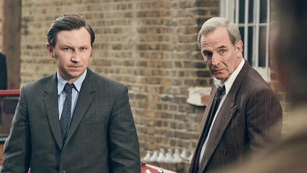 Two men in suits stand beside each other, glaring at a blurred figure in the foreground.