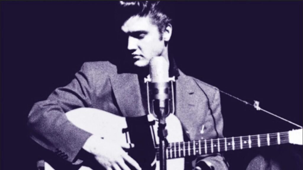 Elvis Presley playing guitar with a mic in front of him