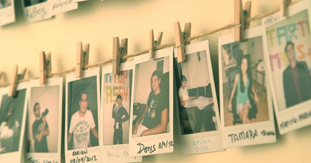 Polaroid pictures of different, smiling people are hung in a line by clothespins. Each portrait has a name and a date written below.