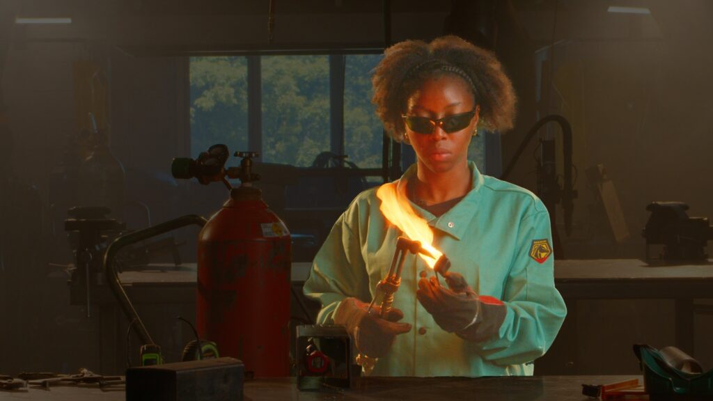 The image shows a person using a handheld torch to work with flame in a workshop setting.