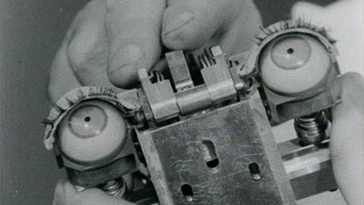 This black and white photo shoes a hand holding a robotic form with two plastic eyeballs.