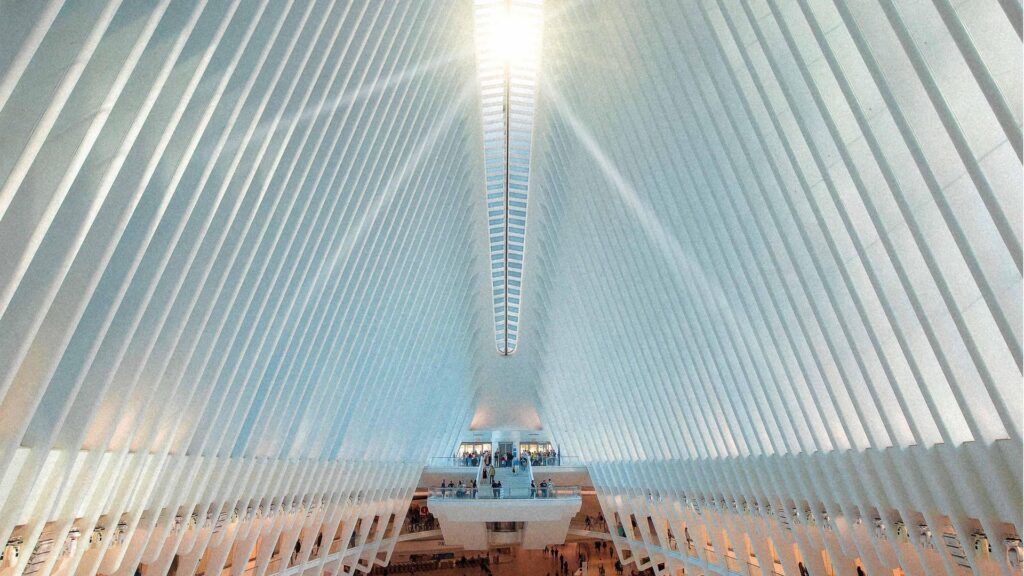 The grand Rafters of the Oculus World Trade Center reach high into the sky, framing the sun as it peaks through the ceiling and shines its rays on the people below.