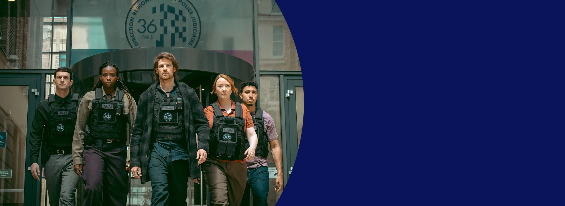 A group of people in bulletproof vests stands in a V-formation as they dramatically walk towards the camera.