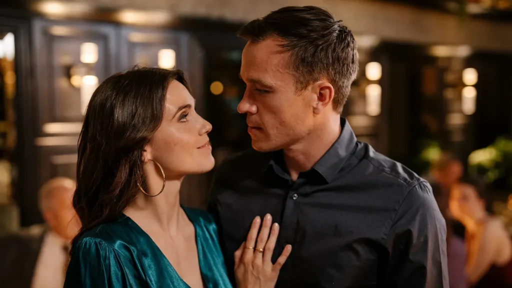 A young man and woman gaze into each others eyes as the woman places her hand on the mans chest. The background is blurred.